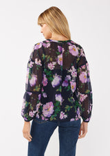 [Color: Navy/Lilac] A back facing image of a blonde model wearing a navy and purple floral print blouse crafted in lightweight chiffon. This boho chic blouse features a split v-neckline with a lace up front, long sleeves, and a relaxed fit. Perfect for special occasions and dinner dates. 