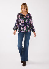 [Color: Navy/Lilac] A front facing image of a blonde model wearing a navy and purple floral print blouse crafted in lightweight chiffon. This boho chic blouse features a split v-neckline with a lace up front, long sleeves, and a relaxed fit. Perfect for special occasions and dinner dates. 