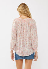 [Color: Natural/Dusty Pink] A back facing image of a blond model wearing a classic v-neck bohemian blouse with a pink abstract print, smocked neckline and cuffs, and button front. 