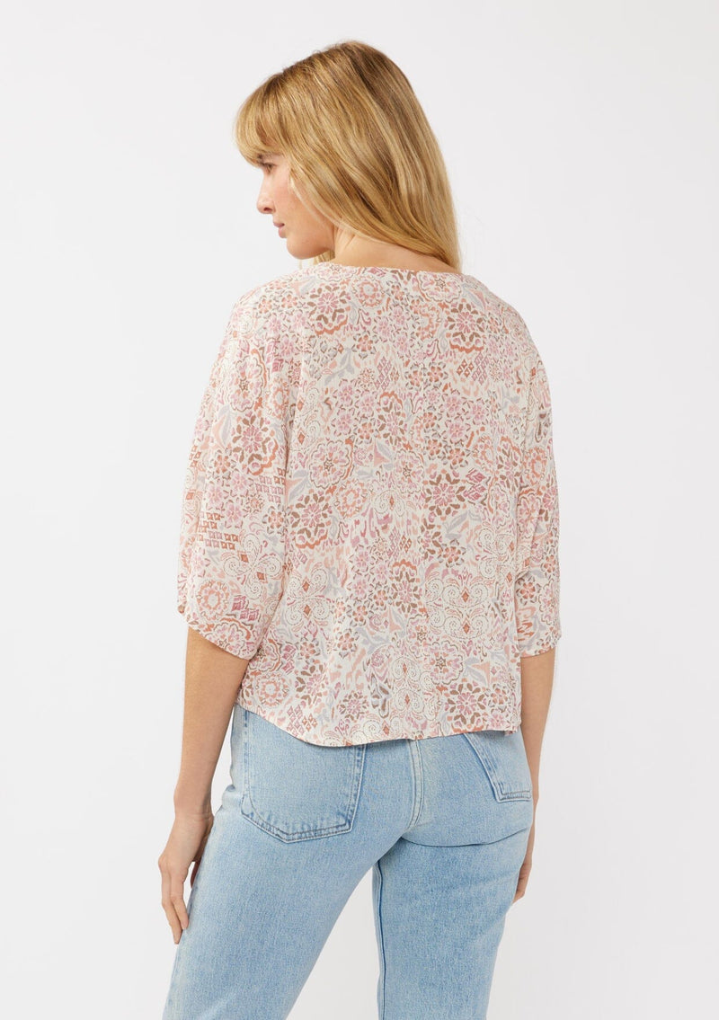 [Color: Natural/Dusty Pink] A back facing image of a blonde model wearing a pink bohemian print blouse with a v-neckline, tie front detail at the hem, and flowy kimono sleeves. Perfect for resort styling and casual outings. 