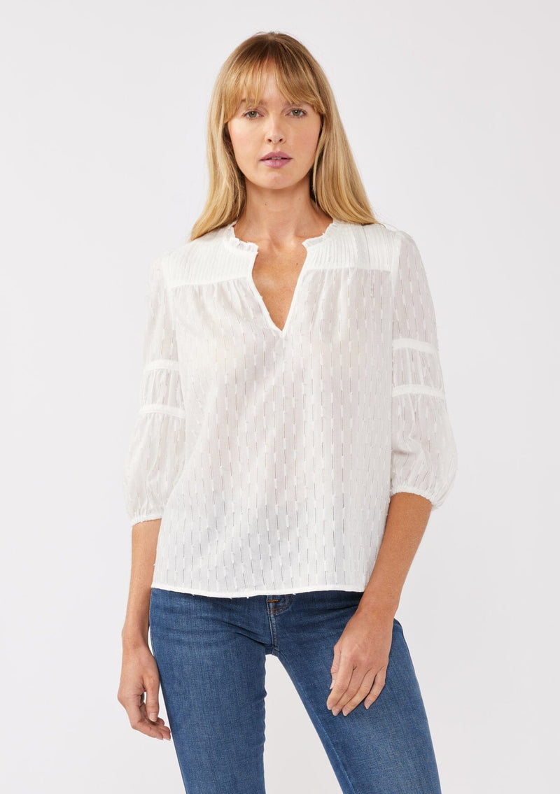 [Color: White] A front-facing image of a blonde model wearing a bohemian white blouse featuring a stripe clip jacquard pattern. This lightweight blouse includes a pintuck yoke, 3/4 length sleeves with tiered details, and a flattering split v-neckline. Ideal for casual outings, it’s a must-have addition to any boho wardrobe.