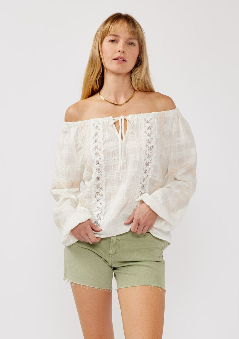 [Color: White/Taupe] A front facing image of a blonde model wearing an off shoulder top crafted in a textured plaid seersucker with an elastic neckline, tie neck detail, long sleeves, lace trim inserts, and contrast embroidery. 