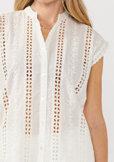 [Color: White] A detail image of a blonde model wearing a white striped eyelet embroidered camp shirt with a button front and short dolman sleeves. Styled for the beach and a resort vacation getaway. 