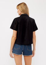 [Color: Black] A back facing image of a blonde model wearing a black floral eyelet shirt in a cropped length. This unbuttoned shirt features a button front, collared neckline, pintuck details, and picot trim. The perfect resort top for layering. 