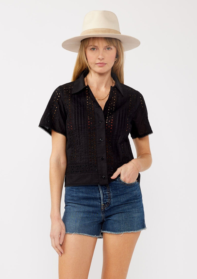 [Color: Black] A front facing image of a blonde model wearing a black floral eyelet shirt in a cropped length. This unbuttoned shirt features a button front, collared neckline, pintuck details, and picot trim. The perfect resort top for layering. 