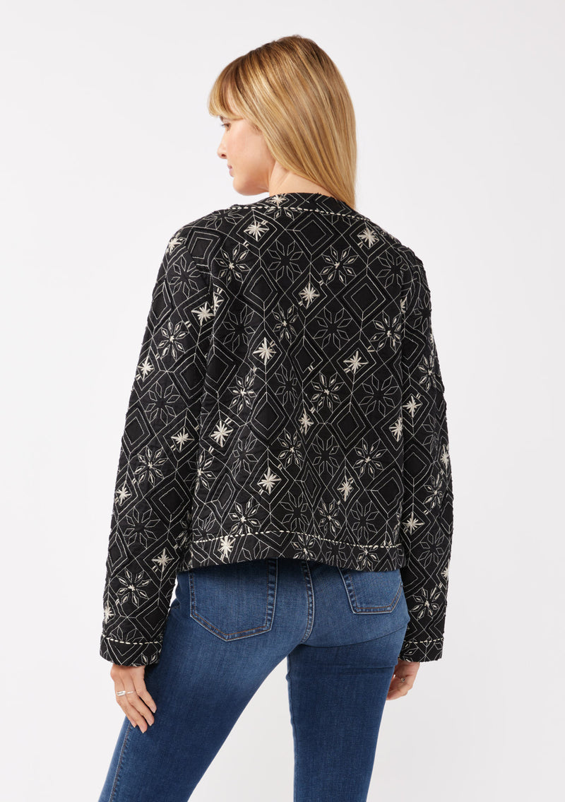 [Color: Black/Taupe] A front facing image of a blonde model wearing a lightweight bohemian spring jacket in black embroidered detail and contrast beige thread detail. With long sleeves, an open front, and a cropped fit.