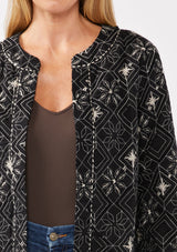 [Color: Black/Taupe] A front facing image of a blonde model wearing a lightweight bohemian spring jacket in black embroidered detail and contrast beige thread detail. With long sleeves, an open front, and a cropped fit.