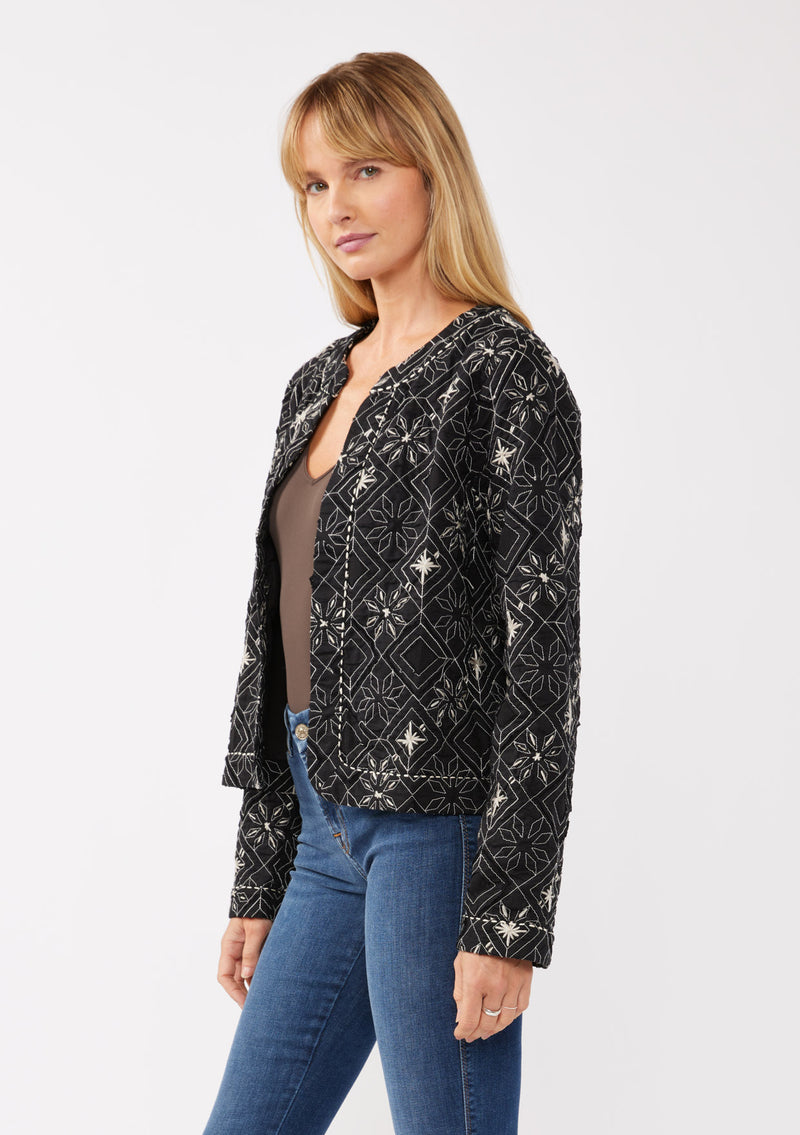 [Color: Black/Taupe] A front facing image of a blonde model wearing a lightweight bohemian spring jacket in black embroidered detail and contrast beige thread detail. With long sleeves, an open front, and a cropped fit.