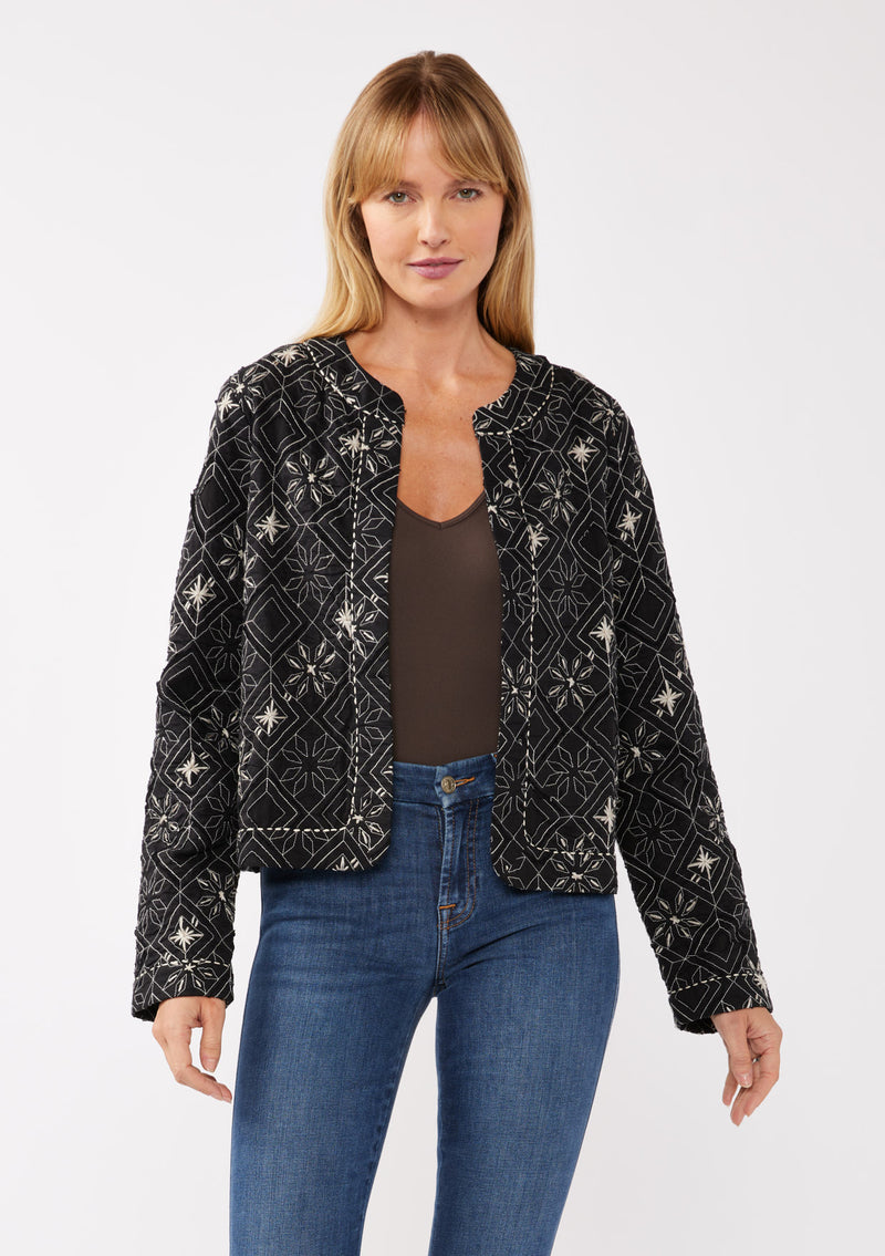 [Color: Black/Taupe] A front facing image of a blonde model wearing a lightweight bohemian spring jacket in black embroidered detail and contrast beige thread detail. With long sleeves, an open front, and a cropped fit.