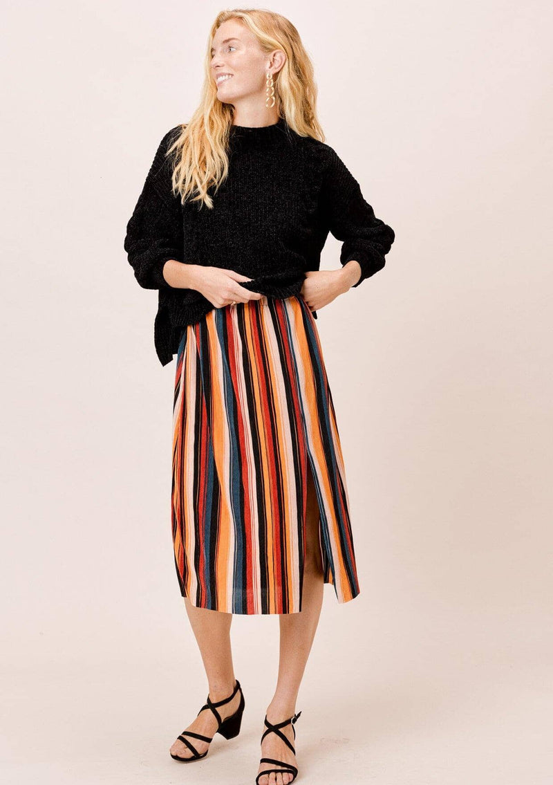 [Color: Black/Spice/Teal:] A blonde wearing a colorful pleated midi skirt with an elastic waistband and front slit. Perfectly versatile, this vertical stripe skirt is styled with a cozy sweater for a laid back look, perfect for the Fall season. 