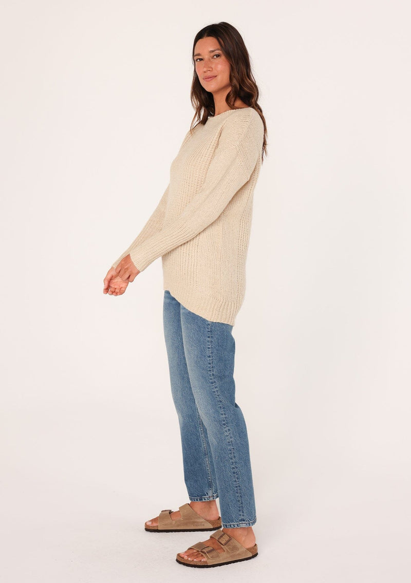 [Color: Natural] A side facing image of a brunette model wearing a high neckline pullover sweater with long sleeves and ribbed details. 