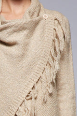 [Color: Oatmeal] A detail image of a brunette model wearing a cozy one-sided fringe sweater cardigan with a versatile wrap front. This asymmetrical sweater features two side buttons for easy draping and securing the wrap silhouette. 