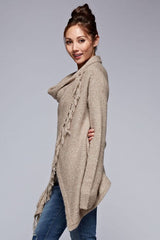 [Color: Taupe] A side facing image of a brunette model wearing a cozy one-sided fringe sweater cardigan with a versatile wrap front. This asymmetrical sweater features two side buttons for easy draping and securing the wrap silhouette. 