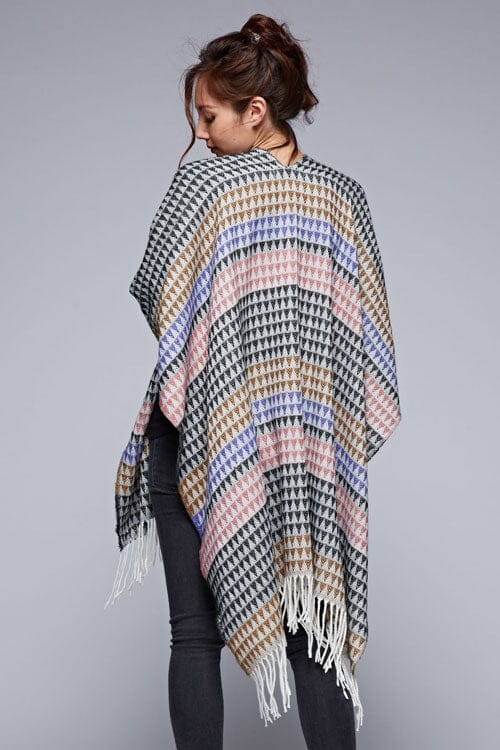 [Color: Black/Natural] A back facing image of a brunette model wearing a geometric stripe knit bohemian poncho with an open front and fringe trim. 