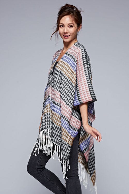 [Color: Black/Natural] A side facing image of a brunette model wearing a geometric stripe knit bohemian poncho with an open front and fringe trim. 