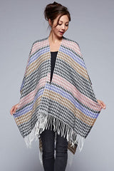 [Color: Black/Natural] A front facing image of a brunette model wearing a geometric stripe knit bohemian poncho with an open front and fringe trim. 