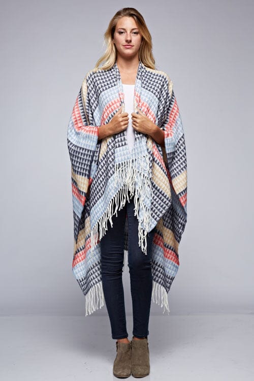 [Color: Navy/Vanilla] A front facing image of a blonde model wearing a geometric stripe knit bohemian poncho with an open front and fringe trim. 