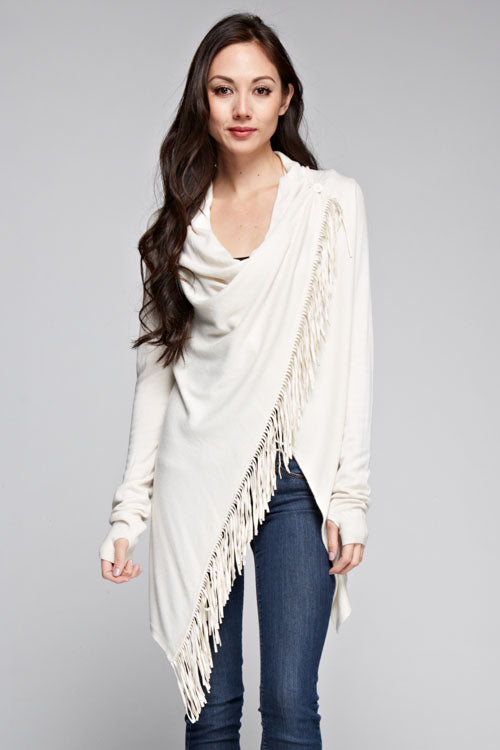 [Color: Vanilla] A brunette model wearing an off white asymmetrical wrap front cardigan with a suede fringe trim and long sleeves with thumb holes. Perfect for elevating any casual outfit. 