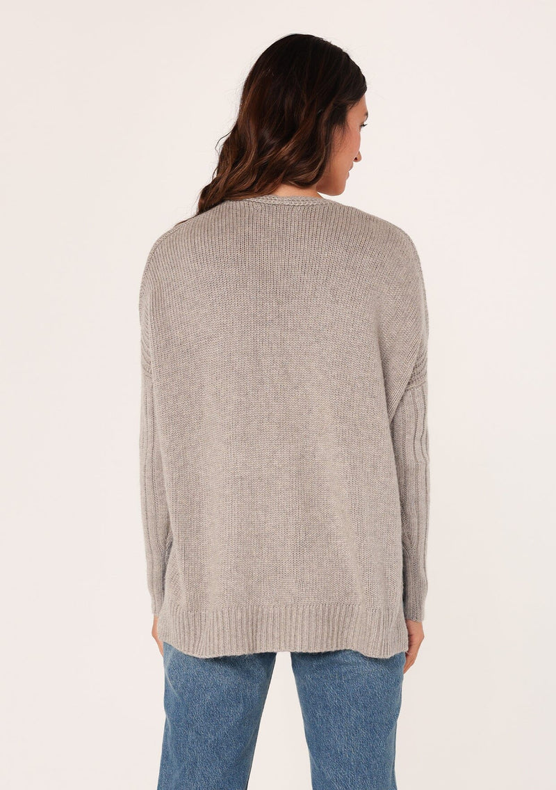 [Color: Heather Grey] A back facing image of a brunette model wearing a cozy grey pullover sweater with a v-neckline, ribbed long sleeves, dropped shoulders, and side vents. The perfect throw on for fall styling. 