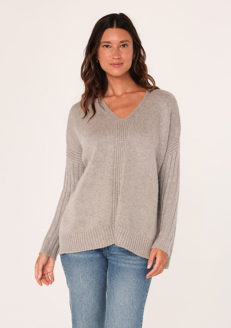 [Color: Heather Grey] A front facing image of a brunette model wearing a cozy grey pullover sweater with a v-neckline, ribbed long sleeves, dropped shoulders, and side vents. The perfect throw on for fall styling. 