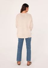 [Color: Heather Petal] A back facing image of a brunette model wearing a cozy grey pullover sweater with a v-neckline, ribbed long sleeves, dropped shoulders, and side vents. The perfect throw on for fall styling. 