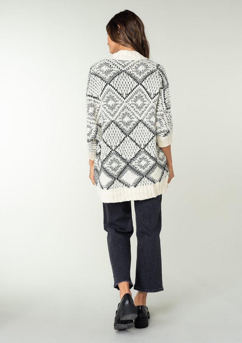 [Color: Ivory/Black] A brunette model wearing a diamond knit pattern cardigan with an open front, 3/4 length sleeves, and a ribbed trim. A cozy knit throw on for the Fall season. 