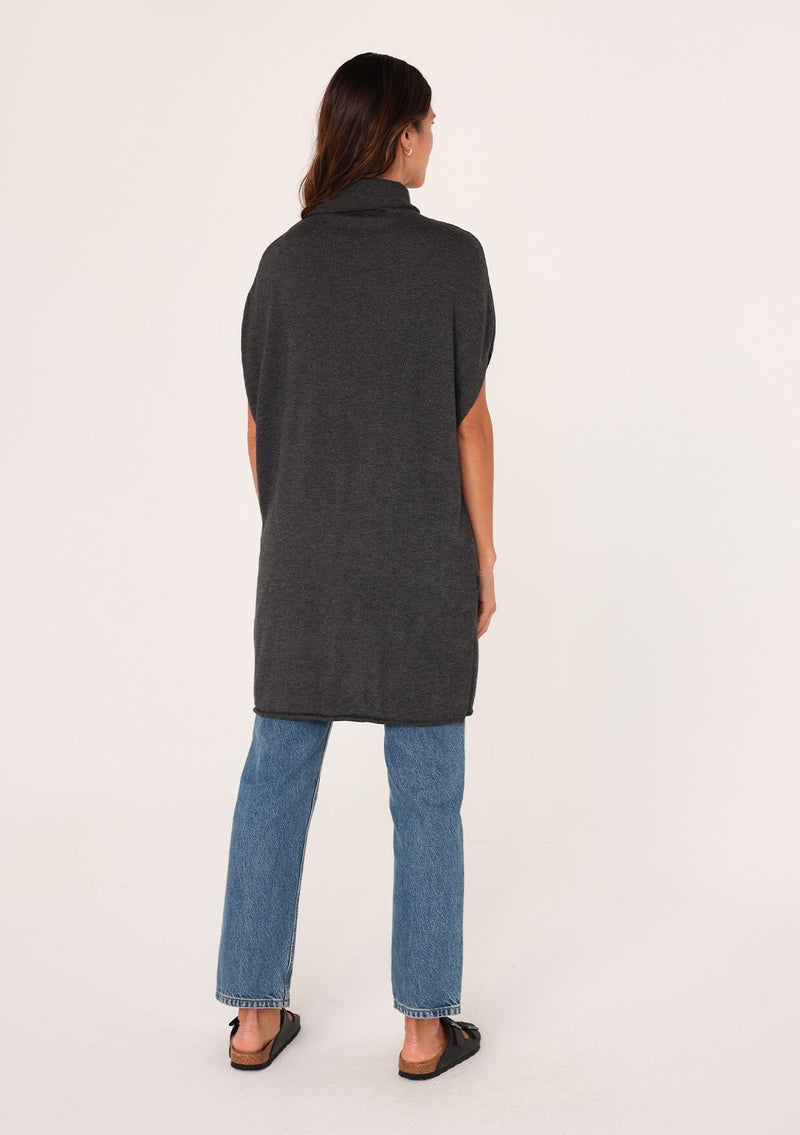 [Color: Dark Heather Grey] A back facing image of a brunette model wearing a dark grey funnel neck tunic sweater with short dolman sleeves, a long hemline, and side slits. The perfect lightweight sweater tunic for layering or wearing on its own as a dress. 