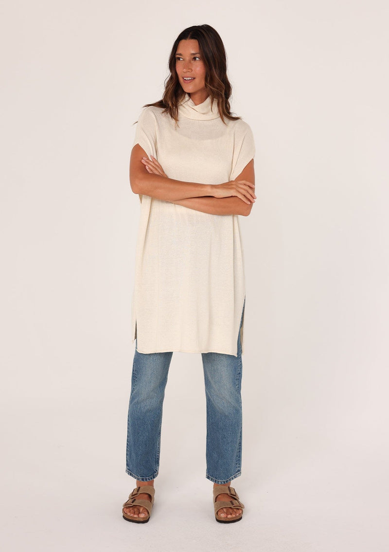 [Color: Oatmeal] A front facing image of a brunette model wearing a off white funnel neck tunic sweater with short dolman sleeves, a long hemline, and side slits. The perfect lightweight sweater tunic for layering or wearing on its own as a dress. 