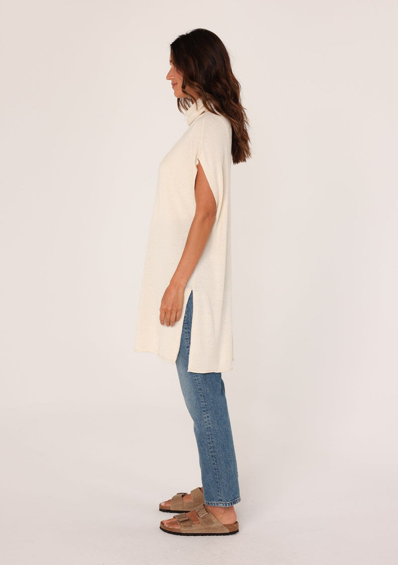 [Color: Oatmeal] A side facing image of a brunette model wearing a off white funnel neck tunic sweater with short dolman sleeves, a long hemline, and side slits. The perfect lightweight sweater tunic for layering or wearing on its own as a dress. 