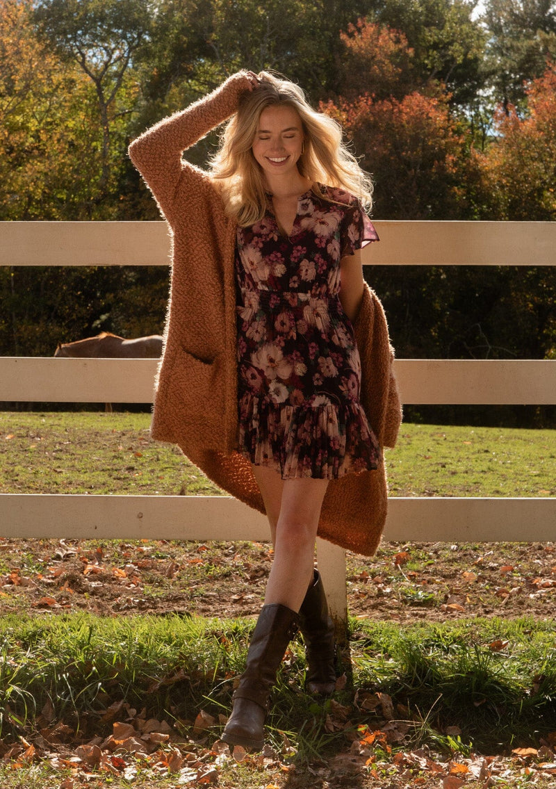 [Color: Camel] A front facing image of a blonde model wearing a fuzzy brown fall cardigan with a popcorn texture at a farm. The cardigan features an open front, large cozy patch pockets, and an attached hoodie, draped for warmth and ideal for layering.