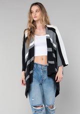 [Color: Charcoal Combo] A blonde model wearing a charcoal combo multi-stripe poncho with an open front, asymmetrical hemline, and a casual, effortless drape in soft acrylic knit.