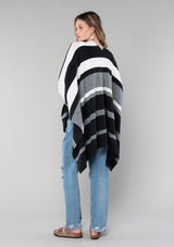 [Color: Charcoal Combo] A blonde model wearing a charcoal combo multi-stripe poncho with an open front, asymmetrical hemline, and a casual, effortless drape in soft acrylic knit.