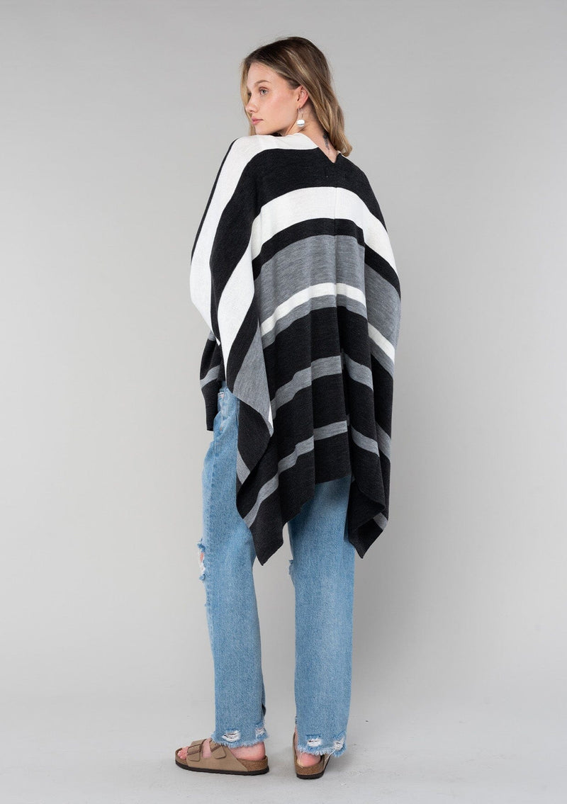 [Color: Charcoal Combo] A blonde model wearing a charcoal combo multi-stripe poncho with an open front, asymmetrical hemline, and a casual, effortless drape in soft acrylic knit.