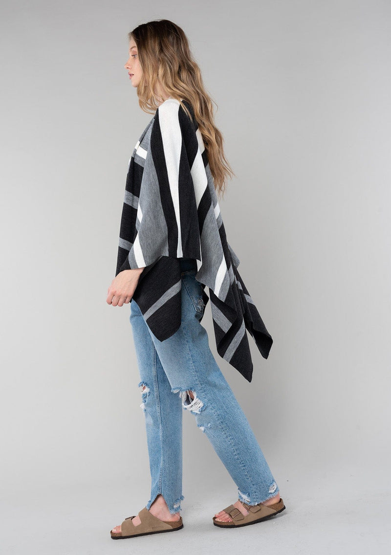 [Color: Charcoal Combo] A blonde model wearing a charcoal combo multi-stripe poncho with an open front, asymmetrical hemline, and a casual, effortless drape in soft acrylic knit.