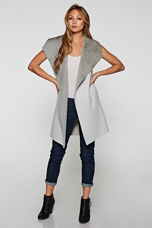 [Color: Grey] A blonde model wearing a casual grey vegan suede vest with a faux fur trim interior and contrasting ribbed knit back. 