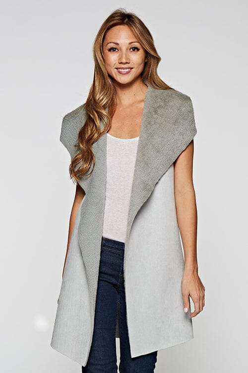 [Color: Grey] A blonde model wearing a casual grey vegan suede vest with a faux fur trim interior and contrasting ribbed knit back. 