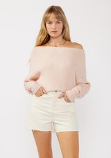 [Color: Heather Blush] A front facing image of a blonde model wearing a light pink waffle knit pullover sweater. With long sleeves, a relaxed fit, and a wide neckline that can be worn off the shoulder.