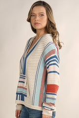 [Color: Natural/Multi] A blonde model wearing a striped knit pullover hoodie with a kangaroo pocket, open knit details, and a v-neckline. Perfect for the beach or casual styling. 