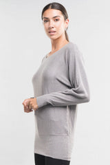 [Color: Heather Ash] A side facing image of a brunette model wearing a relaxed fit pullover grey sweater with long dolman sleeves, a round neckline, and a fitted hem. A long torso sweater perfect for casual outings and lounging. 