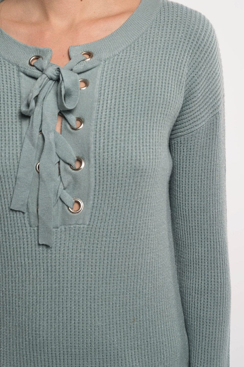 [Color: Pistachio] A detail image of a blonde asian model wearing a mint green pullover sweater featuring a lace-up front and grommet details. This waffle knit sweater is a versatile addition to any fall wardrobe, perfect for everyday wear.