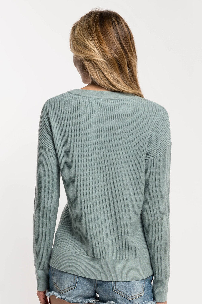 [Color: Pistachio] A back facing image of a blonde Asian model wearing a mint green pullover sweater featuring a lace-up front and grommet details. This waffle knit sweater is a versatile addition to any fall wardrobe, perfect for everyday wear.