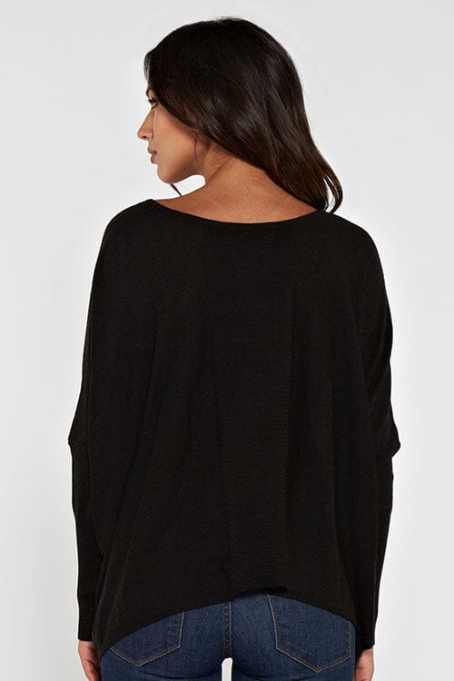 [Color: Black] A brunette model wearing a black cozy throw on pullover with comfortable batwing sleeves. This relaxed fit sweater features a scoop neckline, flowy hem, and rib details at the sleeve and center front. 