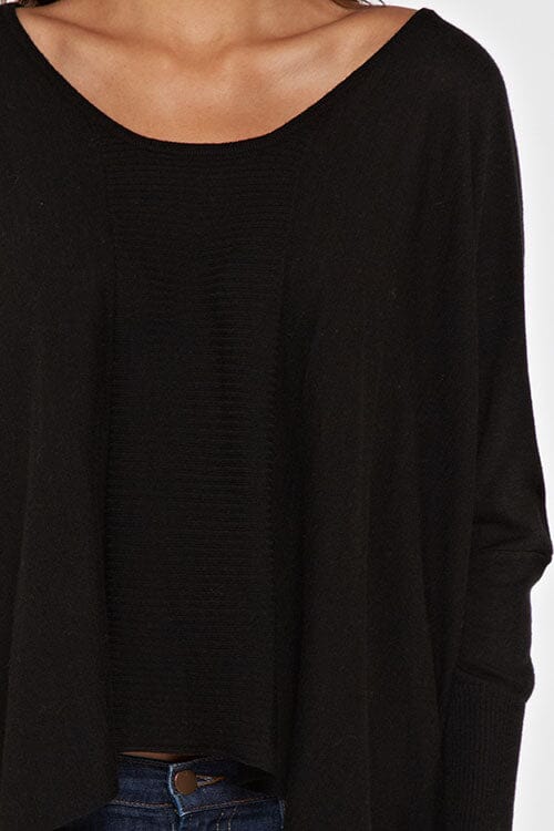 [Color: Black] A brunette model wearing a black cozy throw on pullover with comfortable batwing sleeves. This relaxed fit sweater features a scoop neckline, flowy hem, and rib details at the sleeve and center front. 