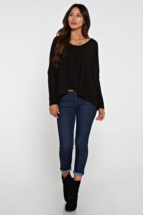 [Color: Black] A brunette model wearing a black cozy throw on pullover with comfortable batwing sleeves. This relaxed fit sweater features a scoop neckline, flowy hem, and rib details at the sleeve and center front. 