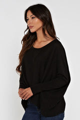 [Color: Black] A brunette model wearing a black cozy throw on pullover with comfortable batwing sleeves. This relaxed fit sweater features a scoop neckline, flowy hem, and rib details at the sleeve and center front. 