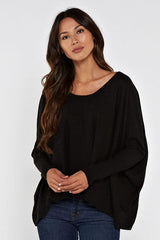 [Color: Black] A brunette model wearing a black cozy throw on pullover with comfortable batwing sleeves. This relaxed fit sweater features a scoop neckline, flowy hem, and rib details at the sleeve and center front. 