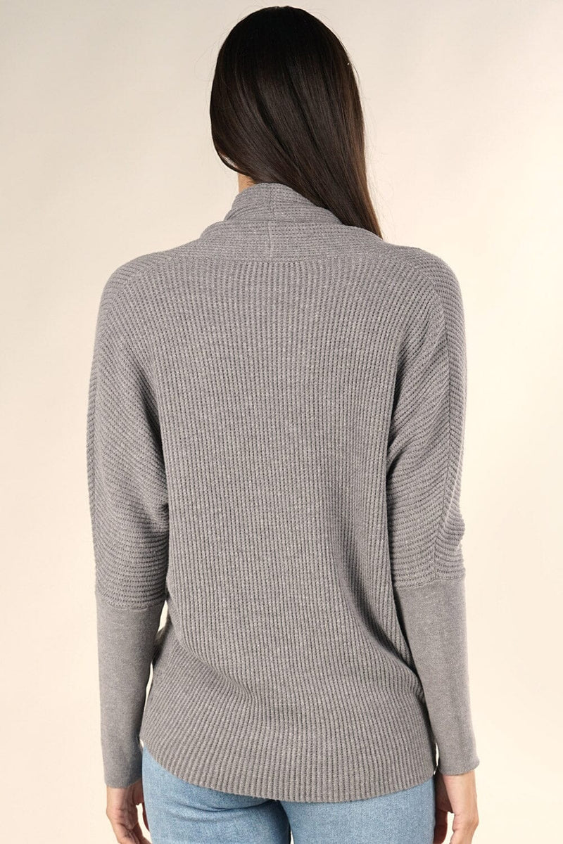 [Color: Heather Ash] A grey waffle knit cross front sweater. Featuring long dolman sleeves, a sexy cross front detail, and a flattering shawl collar that can be worn off the shoulder. Paired here with denim for a classic and chic Fall look. 