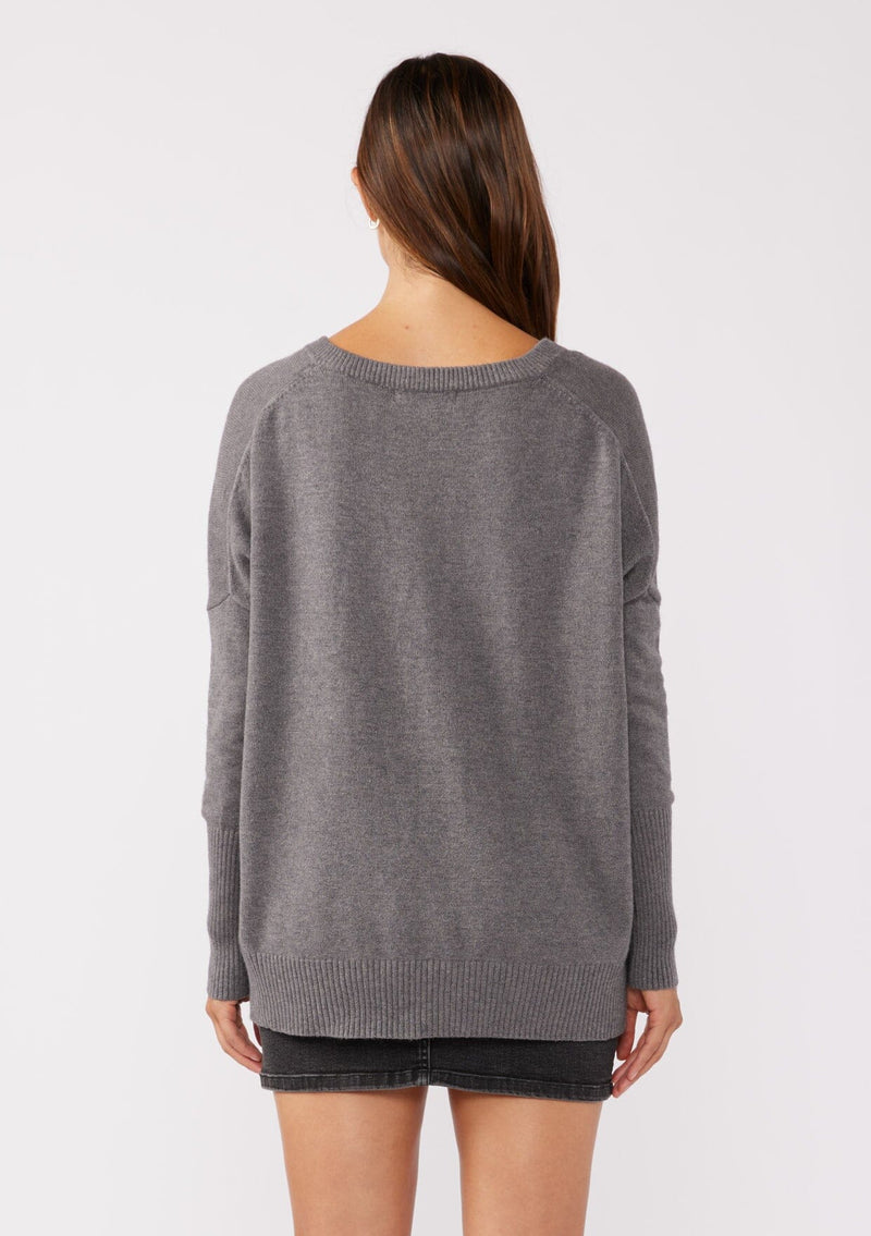 [Color: Heather Charcoal] A back facing image of a brunette model wearing a soft and relaxed fit knit sweater in gray. A cozy fall pullover sweater with a boxy silhouette, v neckline, ribbed trim, and side vents. 