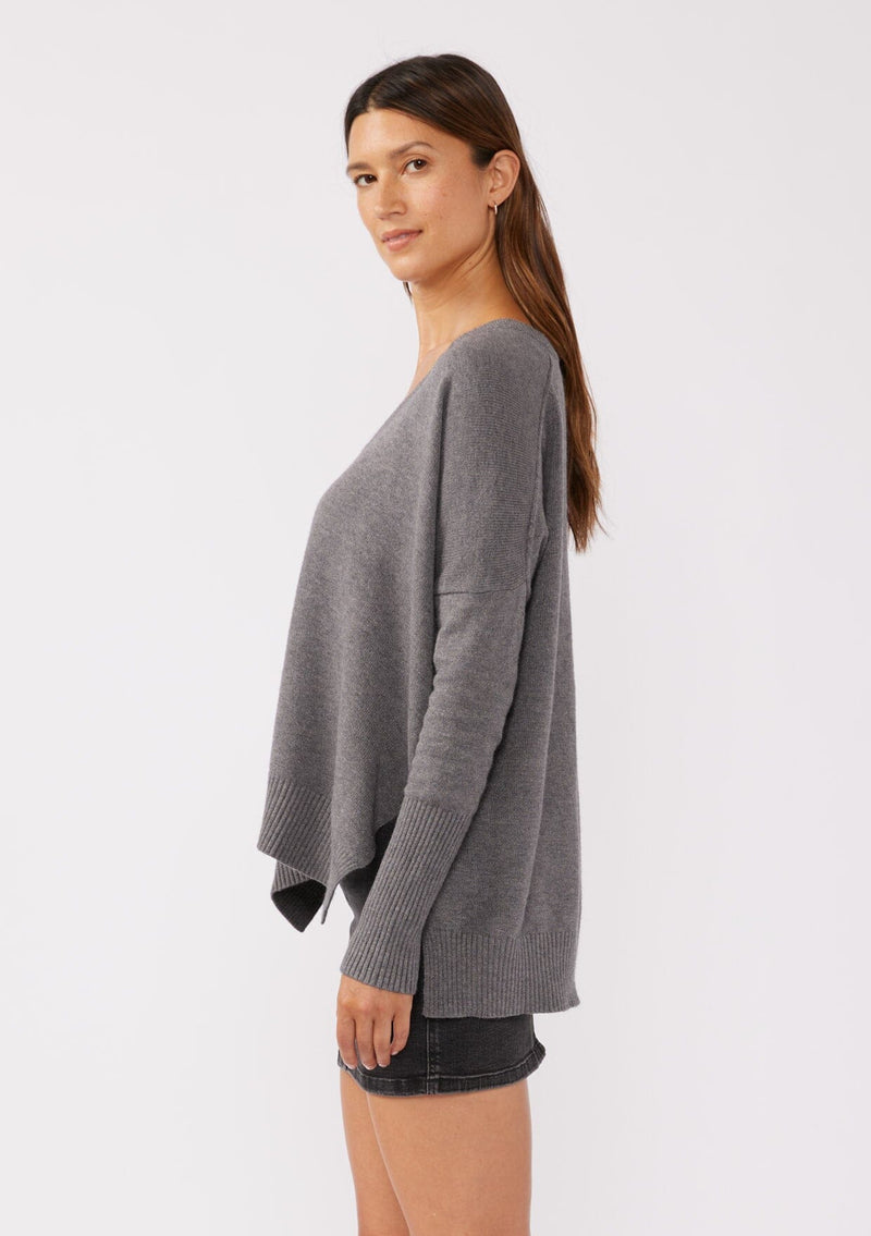 [Color: Heather Charcoal] A side facing image of a brunette model wearing a soft and relaxed fit knit sweater in gray. A cozy fall pullover sweater with a boxy silhouette, v neckline, ribbed trim, and side vents. 