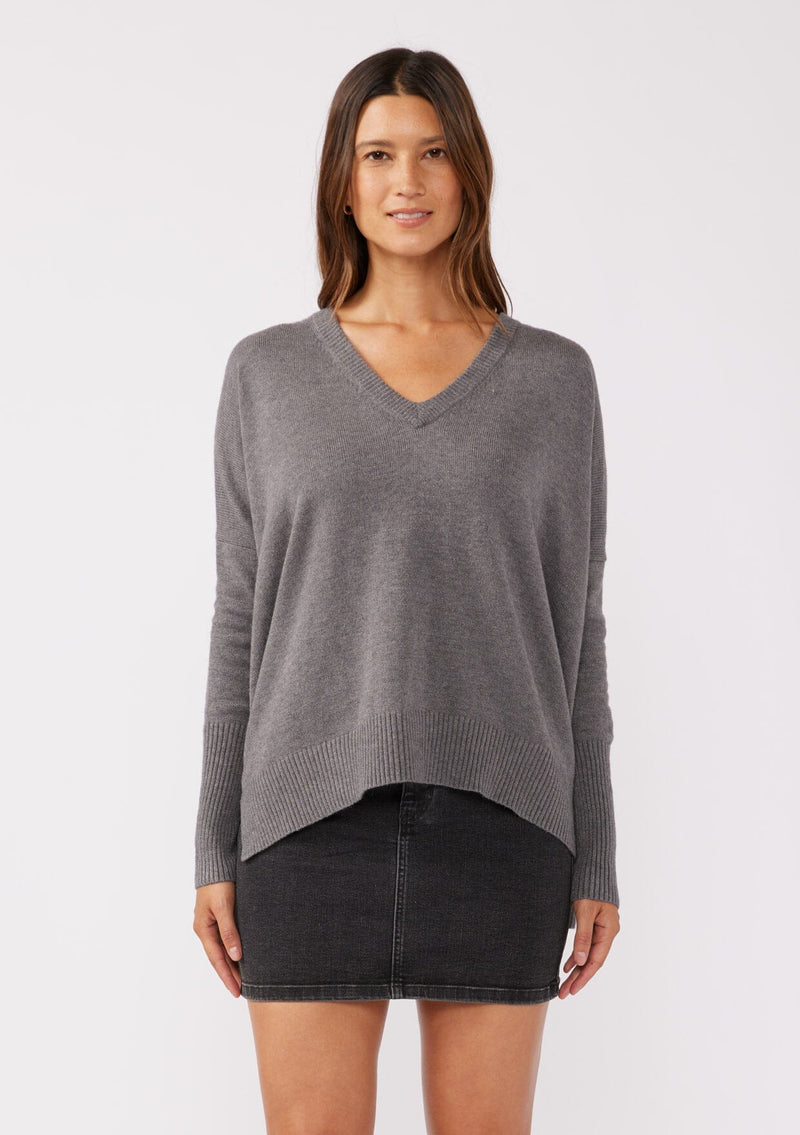 [Color: Heather Charcoal] A front facing image of a brunette model wearing a soft and relaxed fit knit sweater in gray. A cozy fall pullover sweater with a boxy silhouette, v neckline, ribbed trim, and side vents. 